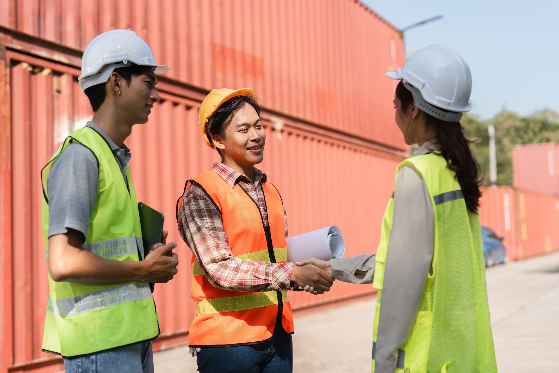 Construction team collaborating and shaking hands over project plans near shipping containers